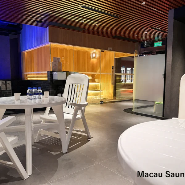 White tables and chairs beside a glass-fronted timber sauna and frosted bathing cubicle